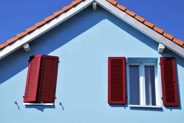 Jasnoniebieska elewacja z czerwoną okiennicą i dachówką. Jaki tynk na elewację sprawdzi się najlepiej?