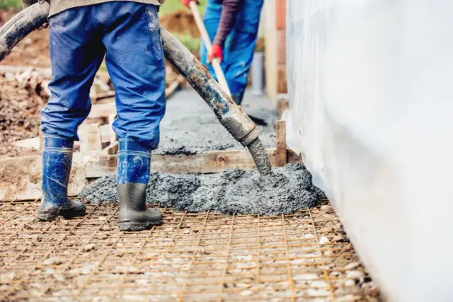 Pracownicy wylewają beton na zbrojenie. Warto wiedzieć, ile waży kubik betonu, by zaplanować prace.